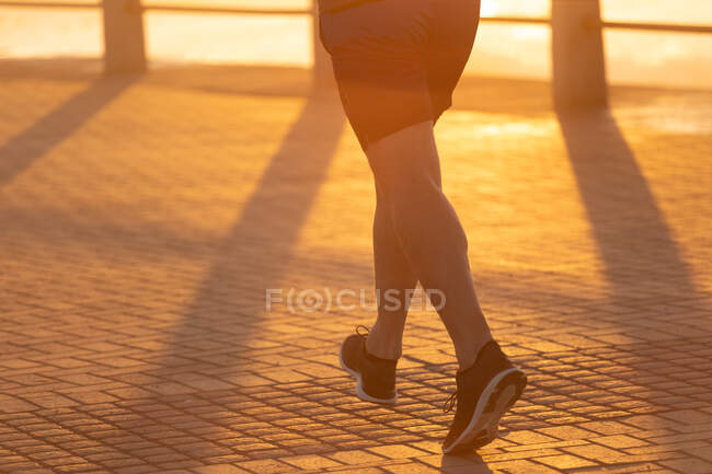 Vista posteriore bassa sezione dell'uomo che si allena su una passeggiata in una giornata di sole, correndo al tramonto — Foto stock