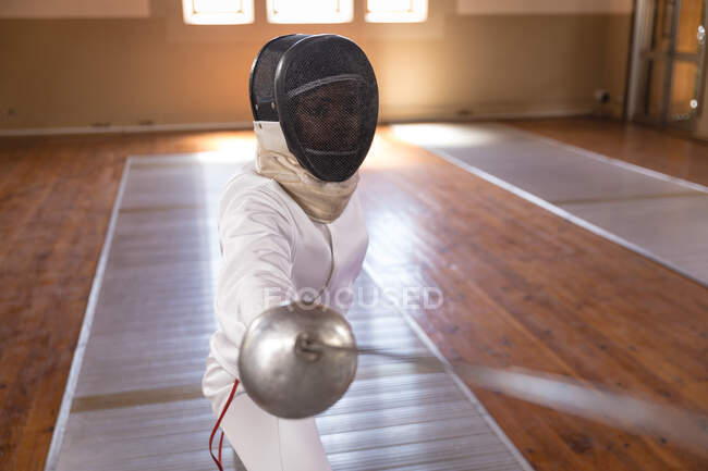 Kaukasische Sportlerin im Fecht-Schutzanzug während eines Fechttrainings, bereitet sich auf ein Duell vor, hält ein Degen und zielt. Fechter beim Training im Fitnessstudio. — Stockfoto