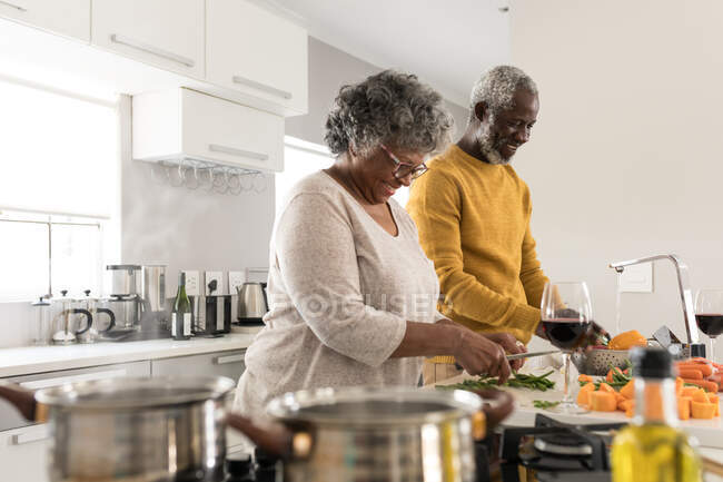 Un couple afro-américain âgé passe du temps à la maison ensemble, la distance sociale et l'isolement personnel en quarantaine pendant l'épidémie de coronavirus covid 19, la préparation de la nourriture, souriant — Photo de stock