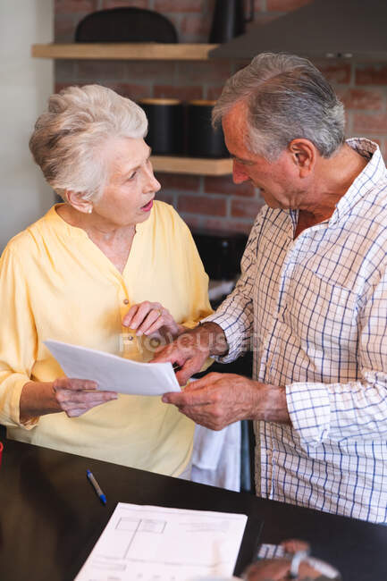 Close up of a retired senior Caucasian couple standing at a table in their dining room looking at paperwork and discussing their finances, at home together isolating during coronavirus covid19 pandemic — Stock Photo