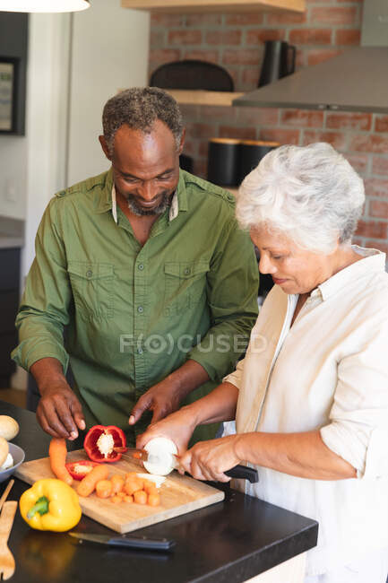 Щаслива подружня пара афроамериканців у відставці вдома, готуючи їжу, розрізуючи овочі на кухні, ізолюючись під час коронавірусної пандемії. — стокове фото