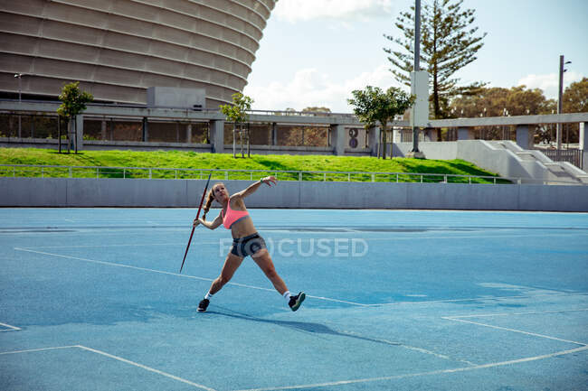 Vue de face d'une athlète blanche pratiquant dans un stade de sport, lançant un javelot. — Photo de stock