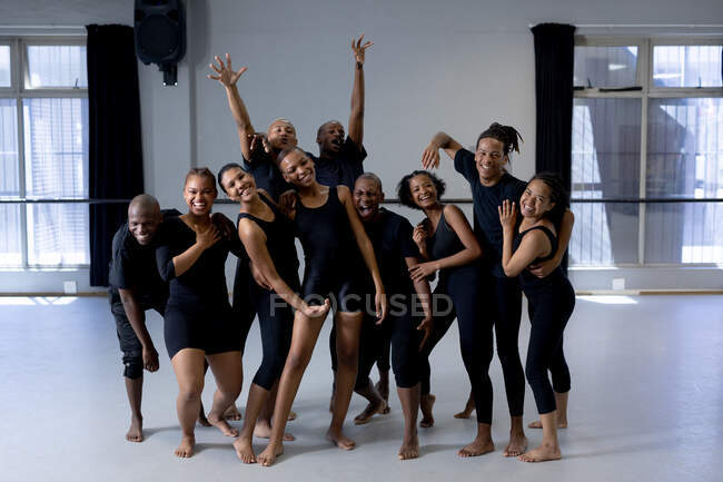 Frontansicht einer multiethnischen Gruppe fitter männlicher und weiblicher moderner Tänzer in schwarzen Outfits, die während eines Tanzkurses in einem hellen Studio eine Tanzroutine üben, zusammen stehen, lächeln und direkt in die Kamera schauen. — Stockfoto