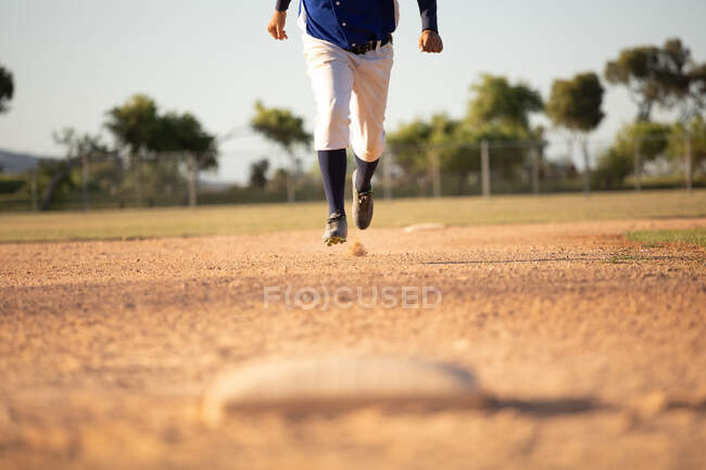 Вид спереду низька секція чоловіка бейсболіста, під час бейсбольної гри в сонячний день, біжить на базу — стокове фото