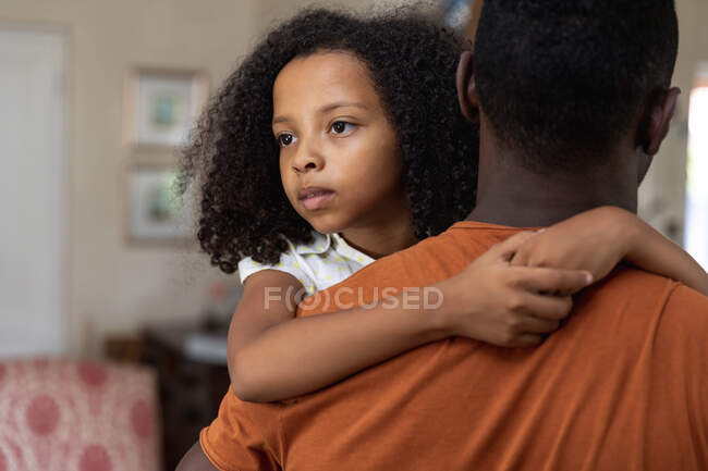 Menina afro-americana, distanciamento social em casa durante o confinamento de quarentena, abraçando seu pai, segurando-a em seus braços . — Fotografia de Stock