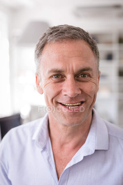 Retrato de cerca de un feliz hombre de negocios caucásico que trabaja en una oficina moderna, mirando directamente a la cámara y sonriendo - foto de stock