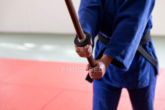 Frontansicht Mittelteil der Judoka mit blauem Judogi, in der Hand einen hölzernen Judo-Jojo-Stock, während eines Judo-Trainings in der Turnhalle stehend. — Stockfoto