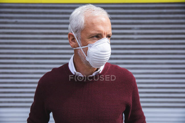 Älterer kaukasischer Mann, der tagsüber auf den Straßen der Stadt unterwegs ist und eine Gesichtsmaske gegen Coronavirus trägt, covid 19. — Stockfoto
