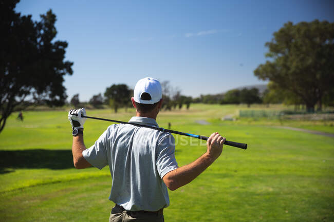 Vista posteriore di un uomo caucasico in un campo da golf in una giornata di sole con cielo blu, tenendo una mazza da golf sulle spalle — Foto stock
