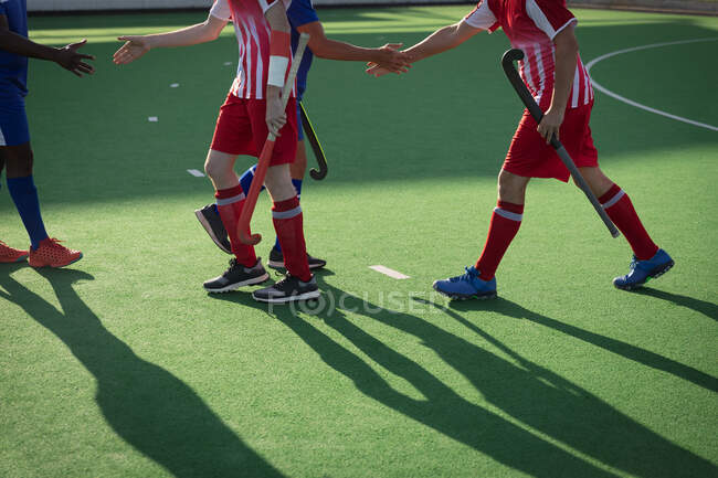 Side view low section of group of male field hockey players from two teams shaking hands, holding hockey sticks on a hockey pitch on a sunny day — Stock Photo