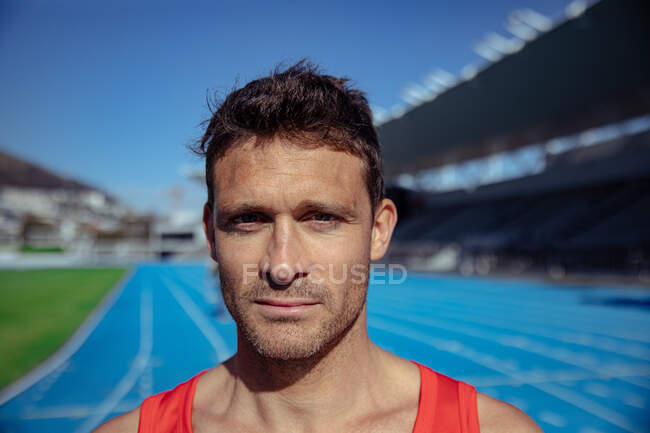 Portrait d'un athlète masculin caucasien confiant portant un gilet rouge pratiquant dans un stade de sport, regardant droit devant la caméra — Photo de stock