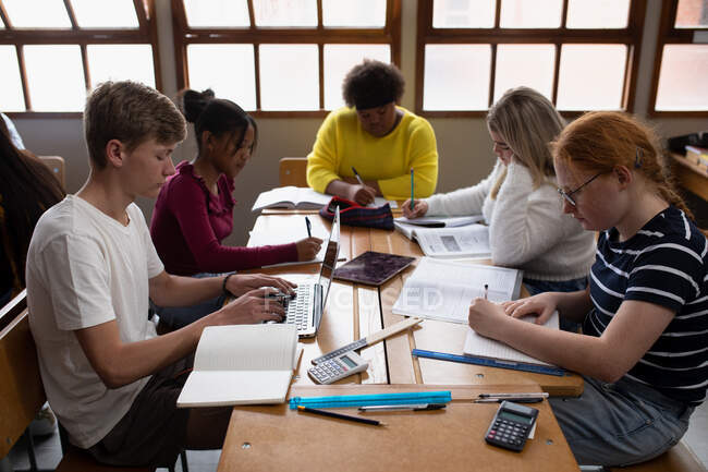 Seitenansicht einer multiethnischen Gruppe von High-School-Teenagern in einem Klassenzimmer, die an einem Tisch sitzen und zusammen arbeiten — Stockfoto