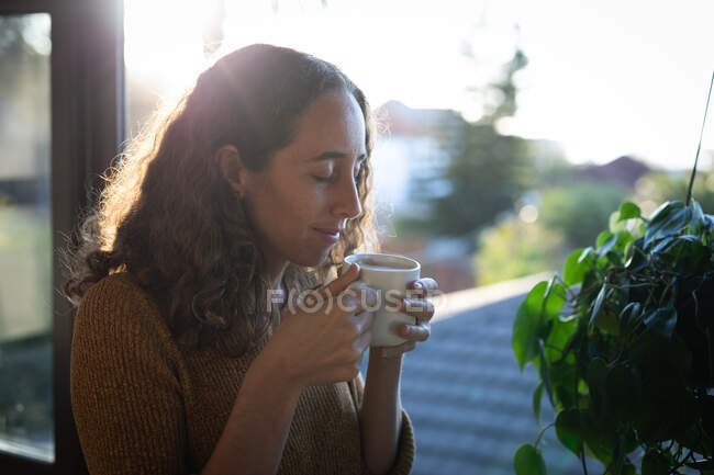 Caucasian woman spending time at home self isolating and social distancing in quarantine lockdown during coronavirus covid 19 epidemic, sitting by the window and having coffee. — Stock Photo