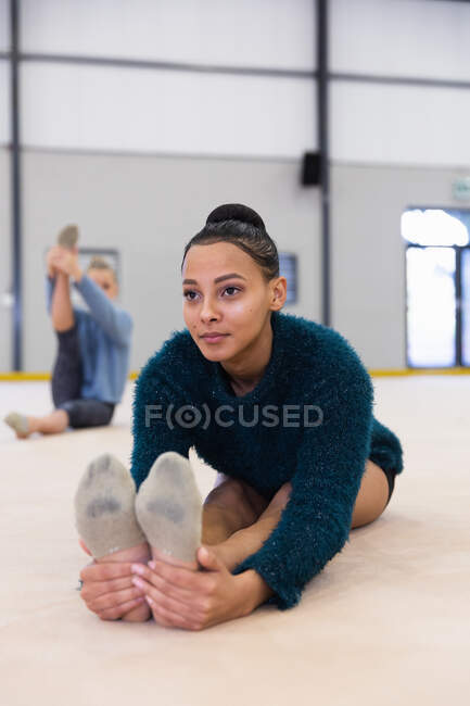 Vista frontal de la raza mixta y gimnastas femeninas adolescentes caucásicas practicando en el gimnasio, estirándose y calentándose. - foto de stock