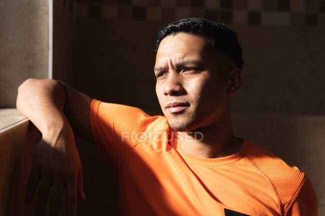 Mixed race male football player wearing sports clothes in changing room during a break in game, resting and thinking looking out of the window. — Stock Photo