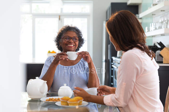 Femme de race mixte senior passant du temps à la maison avec sa fille, distanciation sociale et isolement personnel en quarantaine, prendre le thé ensemble et parler — Photo de stock