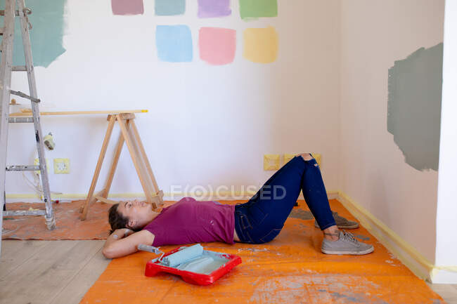 Кавказская женщина проводит время дома, изолируя себя и отдаляясь от общества в карантинной изоляции во время эпидемии коронавирусного ковида 19, отдыхая во время ремонта своего дома, лежа на полу. — стоковое фото