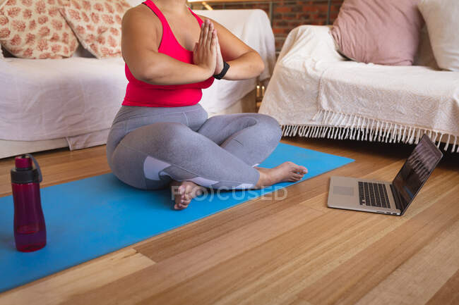 Низкая часть женщины-блогера дома в гостиной, практикует йогу и использует свой ноутбук. Социальное дистанцирование и самоизоляция в карантинной изоляции. — стоковое фото