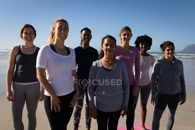 Frontansicht einer multiethnischen Gruppe von Freundinnen, die an einem sonnigen Tag die gemeinsame Zeit am Strand genießen, stehend, in Sportkleidung, lächelnd. — Stockfoto