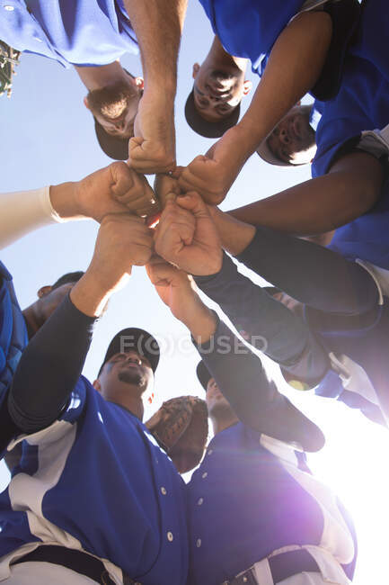 Blick auf ein multiethnisches Team männlicher Baseballspieler, die sich vor einem Spiel vorbereiten, sich in einem Gedränge gegenseitig motivieren und an einem sonnigen Tag eine Hand stapeln — Stockfoto