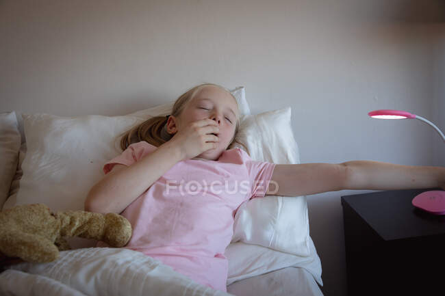 Vista frontal de cerca de una chica caucásica disfrutando de tiempo libre en casa, despertando en su dormitorio, acostada junto a su osito de peluche - foto de stock
