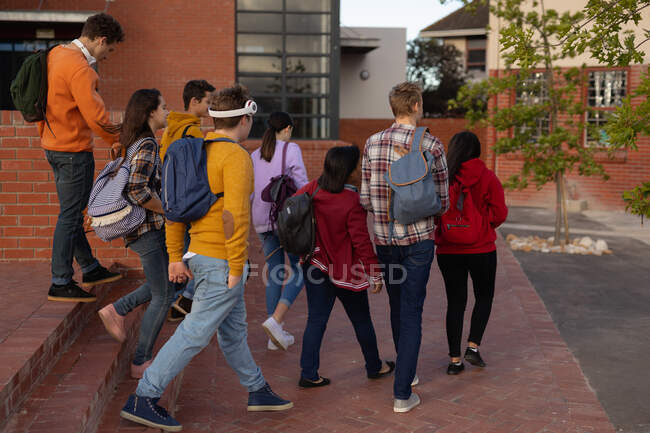 Вид ззаду на багатоетнічну групу студентів-чоловіків і жінок-підлітків, які розмовляють під час прогулянки по шкільних місцях — стокове фото