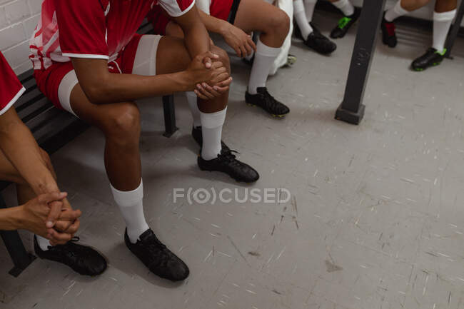 Visão de seção baixa de alto ângulo de um grupo de jogadores de rugby masculinos vestindo faixa de equipe vermelha e branca, sentados e descansando no vestiário após uma partida — Fotografia de Stock