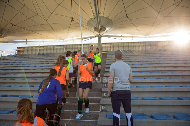 Low angle view of a group of female Caucasian field hockey players and their Caucasian male coach training before a game, running on a stand up and down, on a sunny day — Stock Photo