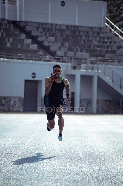 Frontansicht eines gemischten Athleten beim Training in einem Sportstadion, der in Richtung Kamera sprintet. — Stockfoto