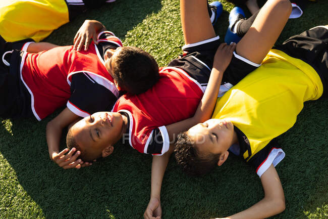 Високий кут зору на багатоетнічну групу хлопчиків-футболістів, які лежать на сонці на ігровому полі, відпочиваючи після тренування — стокове фото