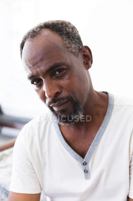 Porträt eines gutaussehenden älteren afroamerikanischen Mannes mit Bart, der ein weißes T-Shirt trägt und mit ernstem Gesichtsausdruck in die Kamera blickt, sich während der Coronavirus-Pandemie selbst isoliert 19 — Stockfoto