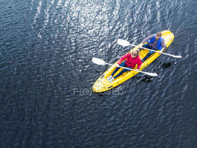 Drone colpo di una coppia caucasica kayak insieme in una barca gialla in acque calme, entrambi pagaiare con remi a doppia estremità — Foto stock
