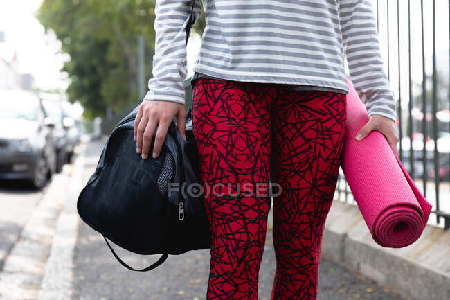 Front view mid section of a fit Caucasian woman on her way to fitness training on a cloudy day, carrying sports bag and a yoga mat — Stock Photo