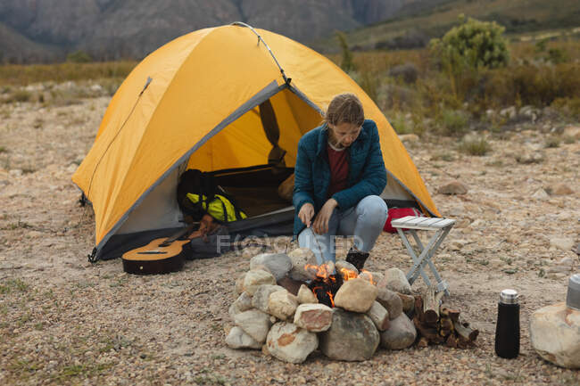 Vorderansicht einer kaukasischen Frau, die eine gute Zeit auf einer Reise in die Berge hat, am Lagerfeuer sitzt und das Feuer beobachtet — Stockfoto