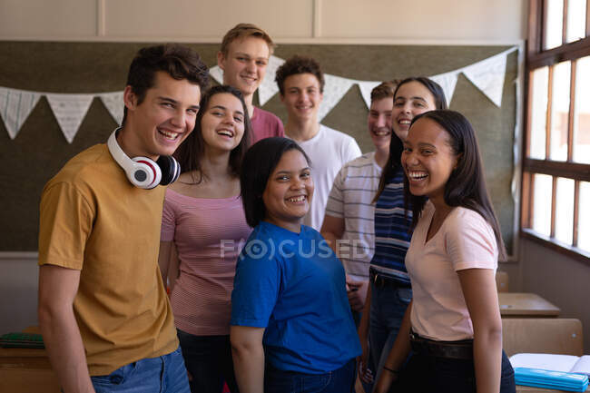 Vista frontale di un gruppo multietnico di alunni adolescenti che si riuniscono in classe e sorridono alla telecamera al momento della pausa — Foto stock