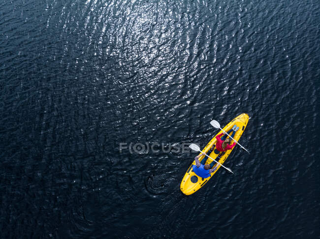 Drone shot of a Caucasian couple kayaking together in a yellow boat on calm water, both paddling with double-ended oars — Stock Photo