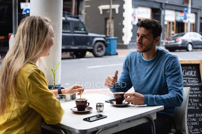 Vista laterale di una coppia caucasica seduta accanto a un tavolo in una terrazza, che prende un caffè, parla e si gode il tempo insieme. — Foto stock