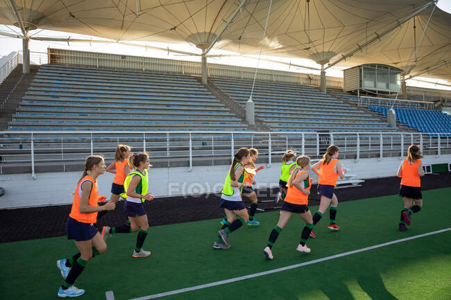 Side view of a group of female Caucasian field hockey players, training before a game, working out on a field hockey pitch, doing exercises, running, on a sunny day — Stock Photo