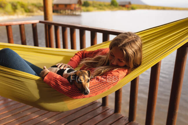 Side view of a Caucasian woman having a good time on a trip to the mountains, lying on a hammock, with a puppy on her belly — Stock Photo