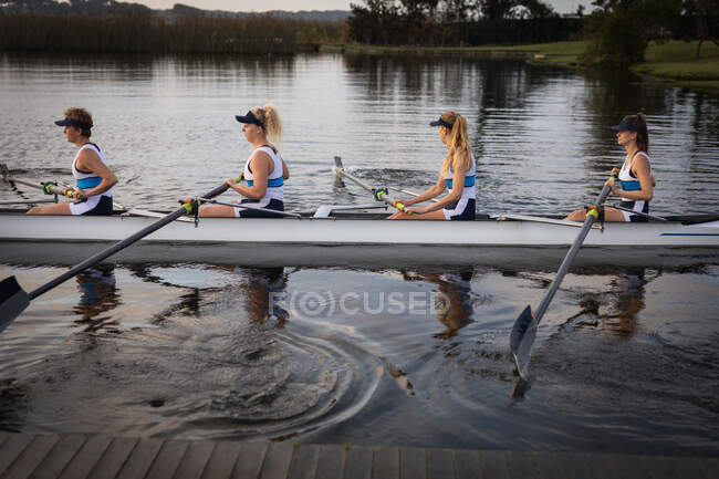 Side view of a rowing team of four Caucasian women training on the river, rowing in a racing shell — Stock Photo