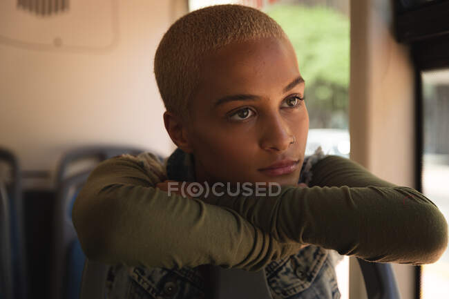 Mixed race alternative woman with short blonde hair out and about in the city, sitting on a bus, leaning on the seat in front, looking out of the window. Independent urban nomad on the go. — Stock Photo