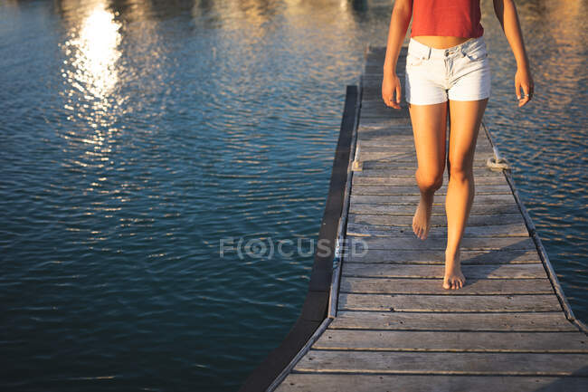 Media sección de chica, disfrutando de su tiempo de vacaciones en el sol por la costa, caminando en un embarcadero - foto de stock