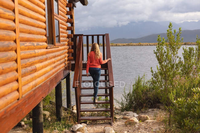 Rückansicht einer kaukasischen Frau, die eine gute Reise in die Berge hat und auf einer Treppe zu einer Hütte geht — Stockfoto
