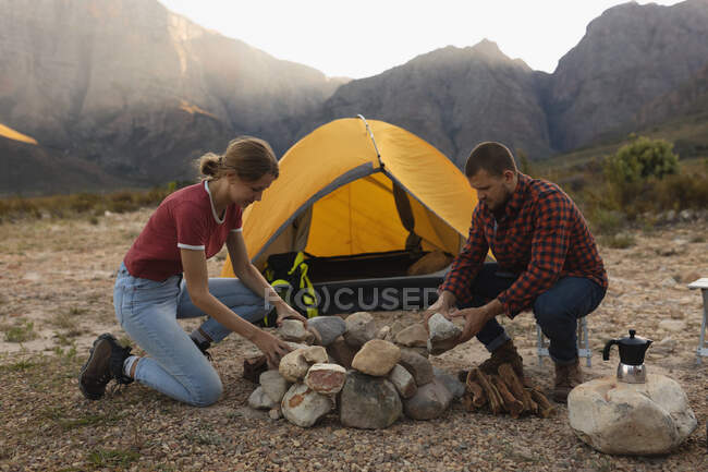 Seitenansicht eines kaukasischen Paares, das eine gute Zeit auf einer Reise in die Berge hat und ein Lagerfeuer baut — Stockfoto