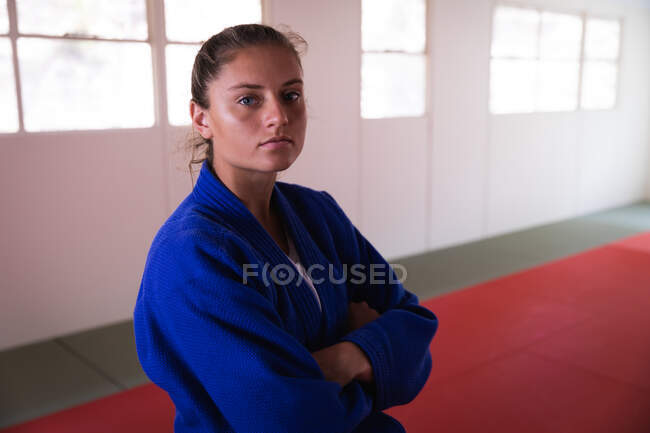 Ritratto di una giovane judoka caucasica sicura di sé con indosso judogi blu, in piedi in palestra con le braccia incrociate e guardando dritto in una macchina fotografica. — Foto stock