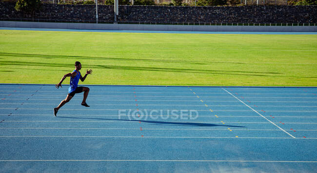 Вид сбоку смешанной расы спортсмен, практикующий на спортивном стадионе, спринтинг. — стоковое фото