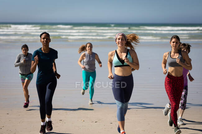 Front view of a multi-ethnic group of female friends enjoying exercising on a beach on a sunny day, running on the seashore. — Stock Photo