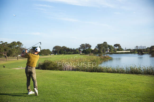 Vista posteriore di un uomo caucasico in un campo da golf in una giornata di sole con cielo blu, colpendo una pallina da golf — Foto stock