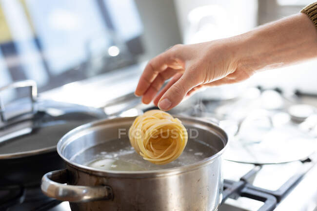 Close up mid section of woman wearing a sweater, cooking pasta for her lunch. Social distancing and self isolation in quarantine lockdown. — Stock Photo