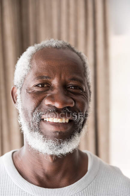 Ritratto di un anziano afroamericano che trascorre del tempo a casa, allontanamento sociale e isolamento in quarantena durante l'epidemia di coronavirus covid 19, guardando la telecamera e sorridendo — Foto stock